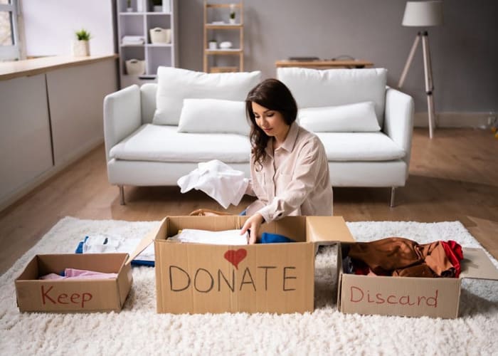 woman decluttering by sorting items into a keep, donate and discard box